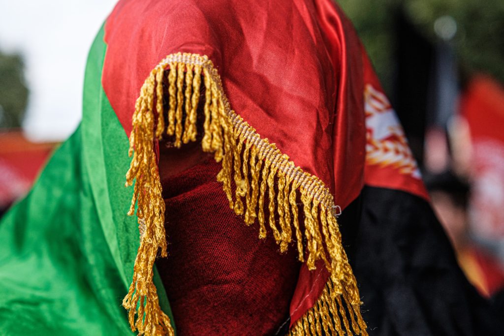 Person's head covered by the Afghan flag with tassels covering their face.